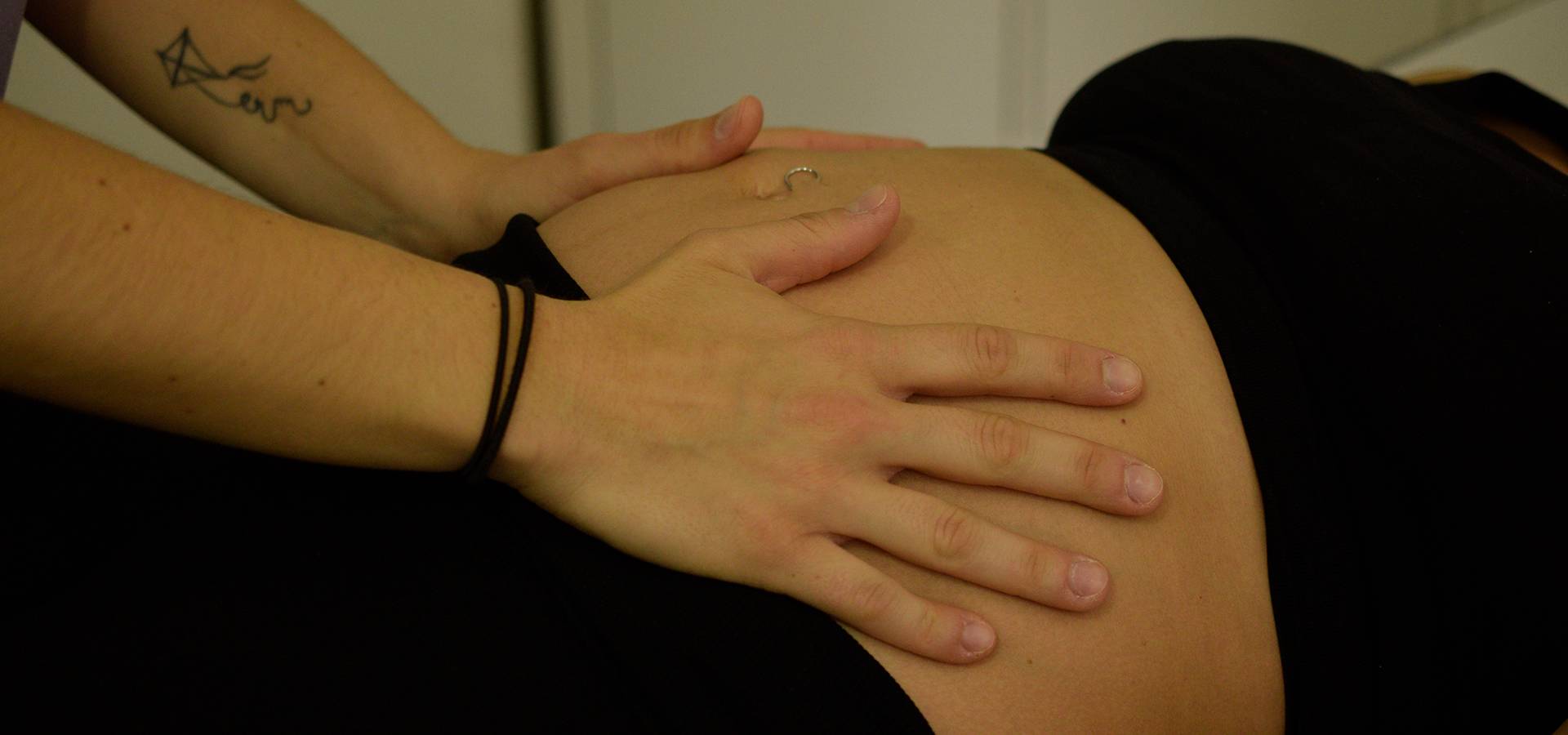 Osteopata Sara Penno durante una seduta di osteopatia esegue una manipolazione delicata sull’addome di una donna in gravidanza distesa su un lettino. Le mani dell’osteopata sono posate sul ventre della paziente che indossa una maglietta nera.